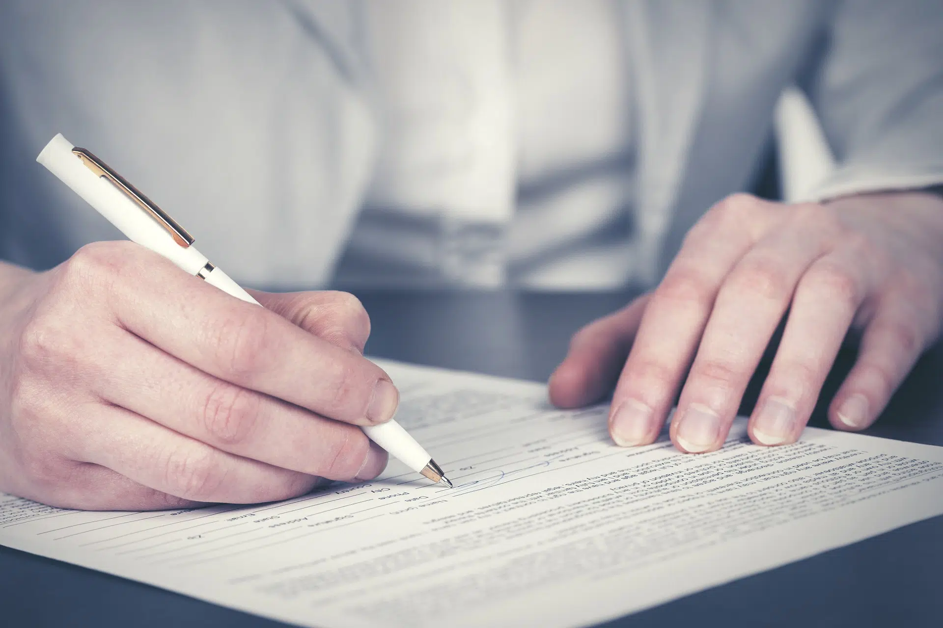 A hand signs a document, another rests on the paper | Domestic Violence Law | The Hemmat Law Group