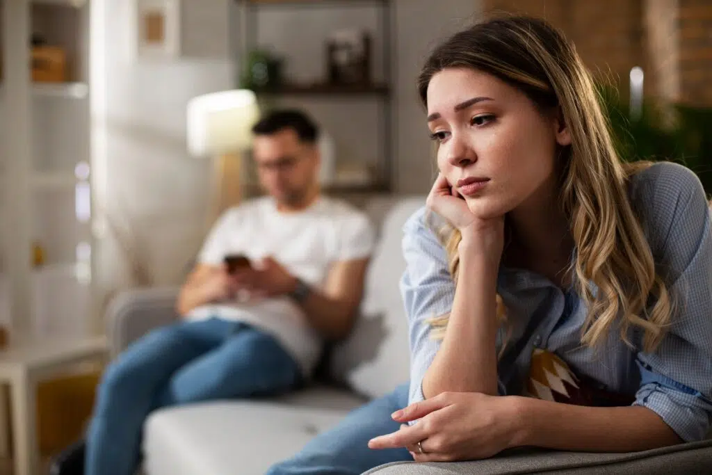 Pensive woman on couch and man nearby on phone | Domestic Violence Law | The Hemmat Law Group