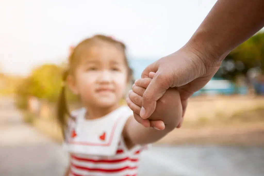 A child in a striped shirt holds hands with an adult | Divorce Lawyer | The Hemmat Law Group