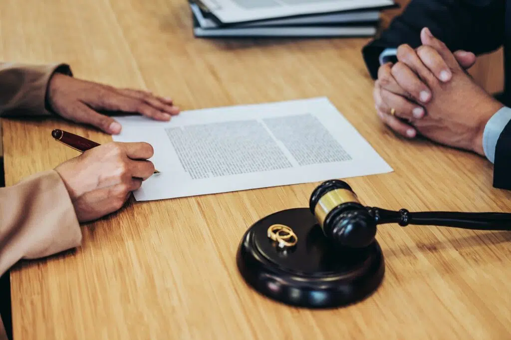 Person signing divorce papers with wedding rings and gavel | Divorce Lawyer | The Hemmat Law Group