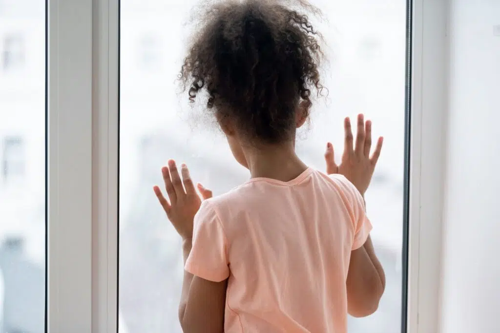A young girl with curly hair gazes out a window | Child Custody Lawyer | The Hemmat Law Group