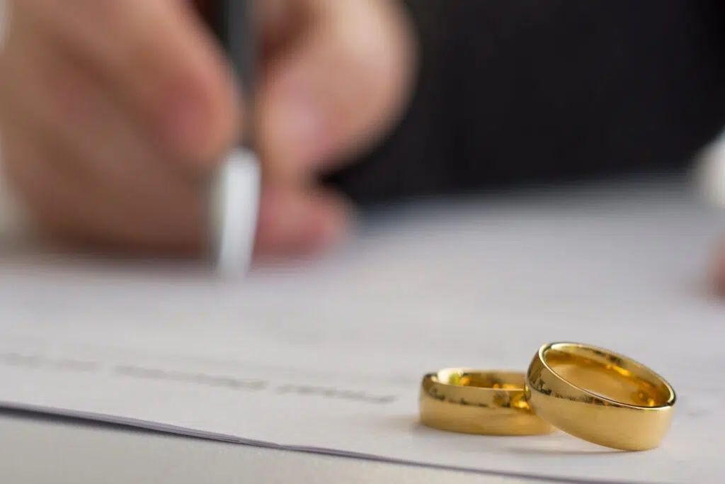 Hand signing divorce papers, wedding rings nearby | Divorce Lawyer Seattle | The Hemmat Law Group