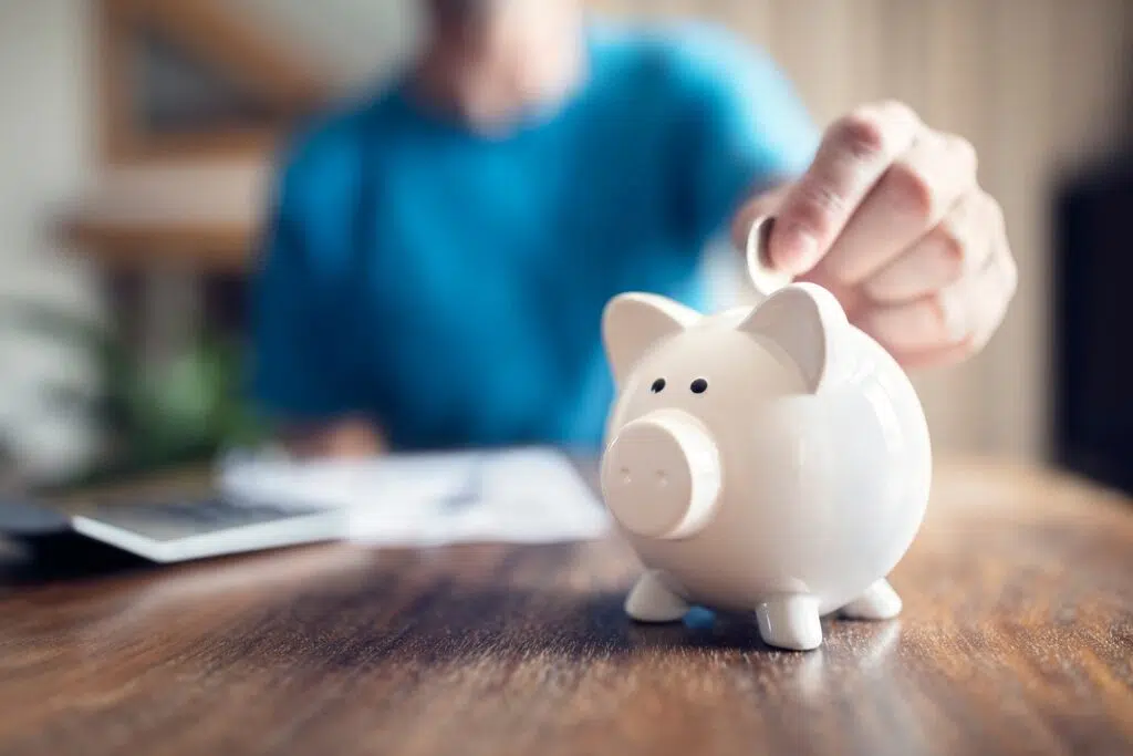 Deposits a coin into a white piggy bank | High Asset Divorce Attorney Seattle | The Hemmat Law Group