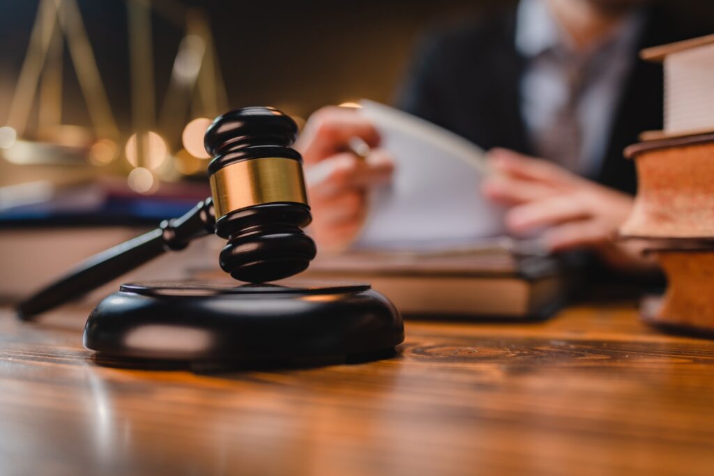 A male attorney in a suit looks at paperwork at a wooden desk in front of a gavel.