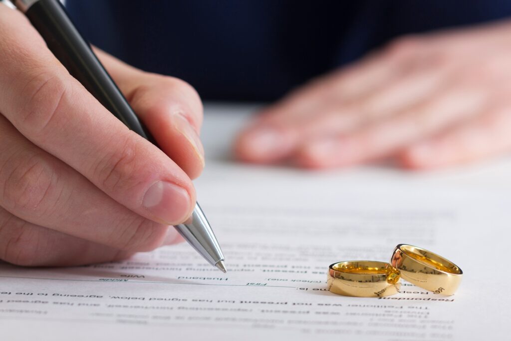 A person writing on a piece of paper with two wedding rings resting on it.