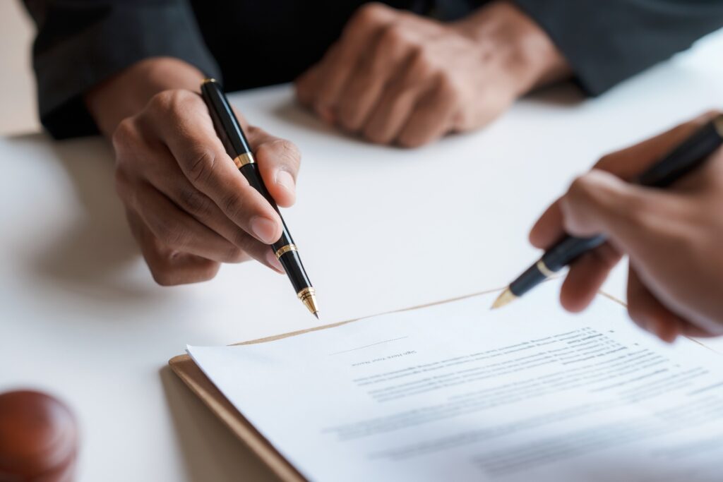 Two hands holding pens pointing toward paperwork on a table.