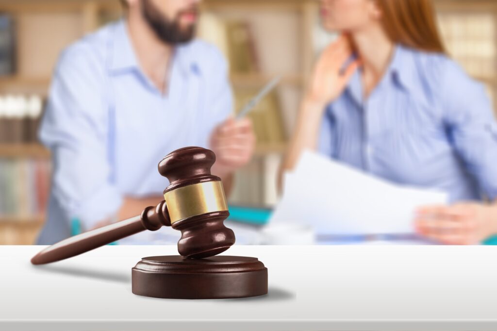 A couple sits at a desk holding paperwork and talking in front of a gavel resting on its stand.