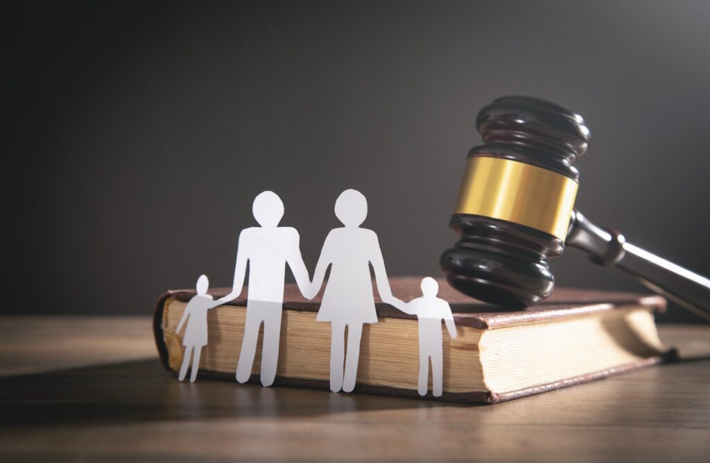 A white paper cutout of a family rests against a law book with a gavel resting on it.