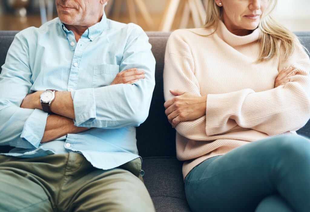 A couple sits side by side on a couch refusing to look at each other.