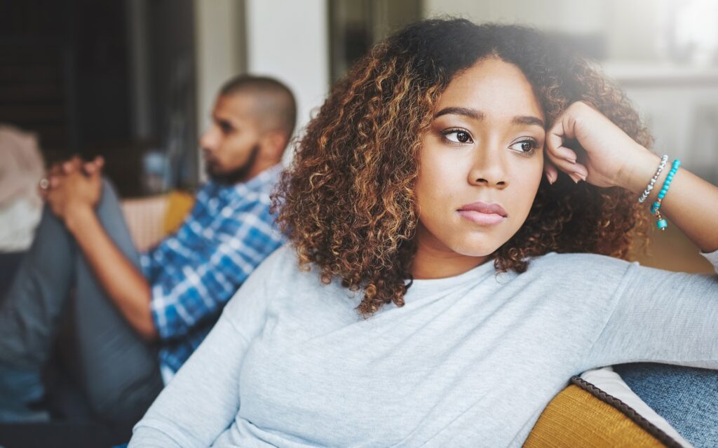 An upset couple sits on a couch with the woman looking off in the distance.