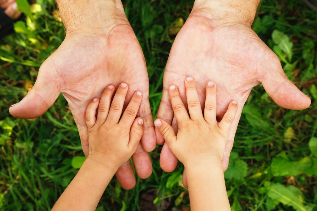 Two childs hands rest on two adult hands above some leaves.