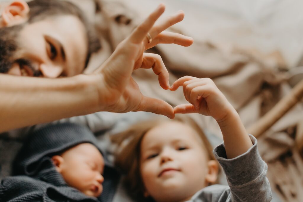 A man laying down with his two children forming a heart with his hand and his child's hand.