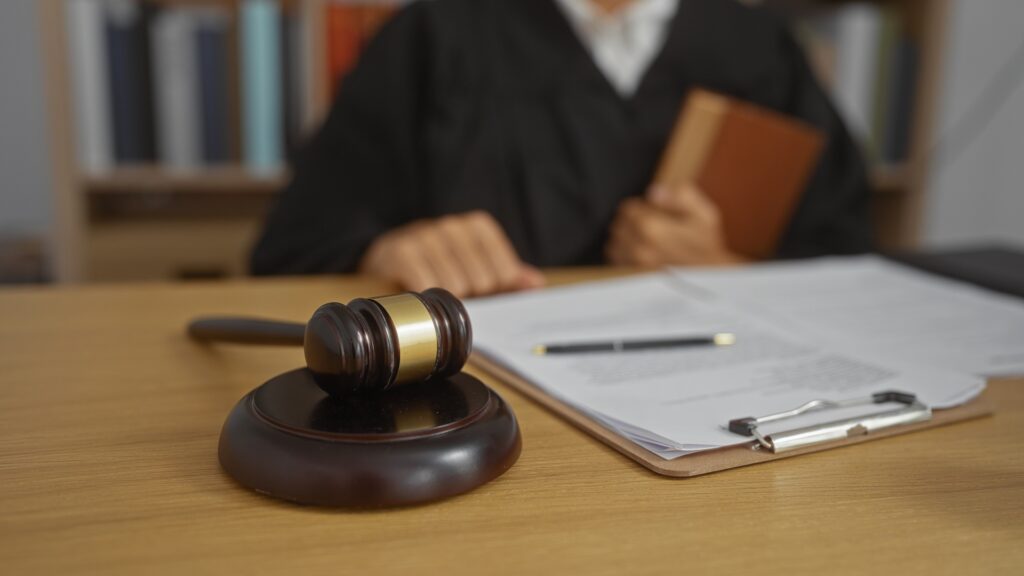 A judge sits at a desk in front of paperwork and a gavel resting on its stand.