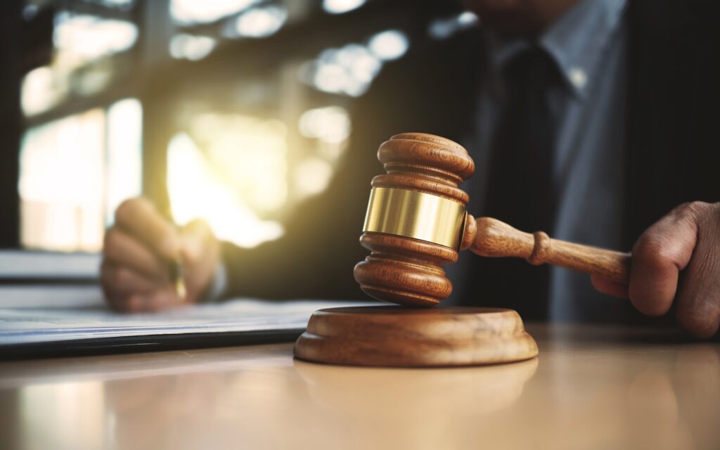 A man writing on some papers holding a gavel that is resting on its stand.