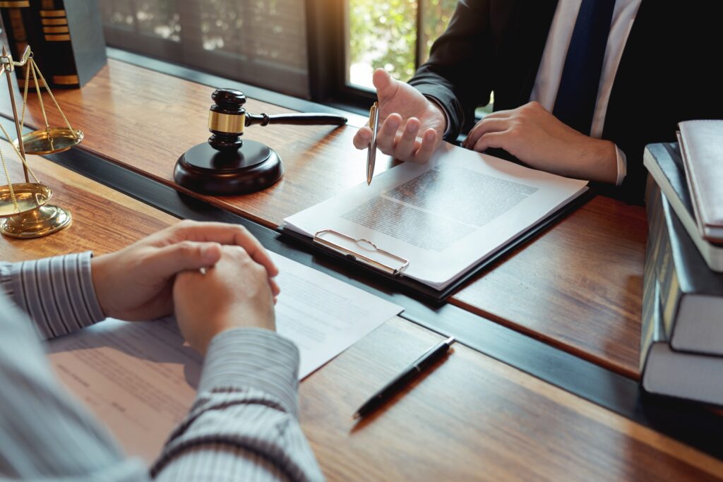 A man sits across from an attorney at a desk in front of papers and a gavel resting on its stand.