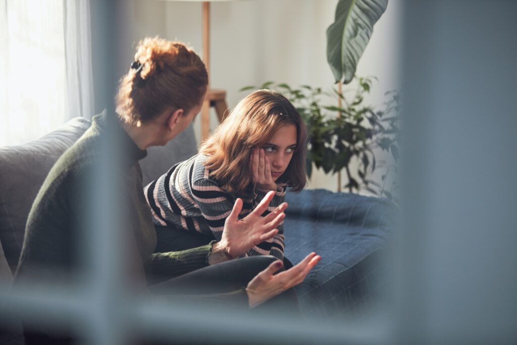 Looking through an interior window at a mother talking with her upset son on a couch.