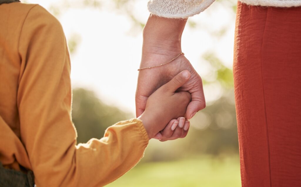 An adult woman holding hands with a child outside.