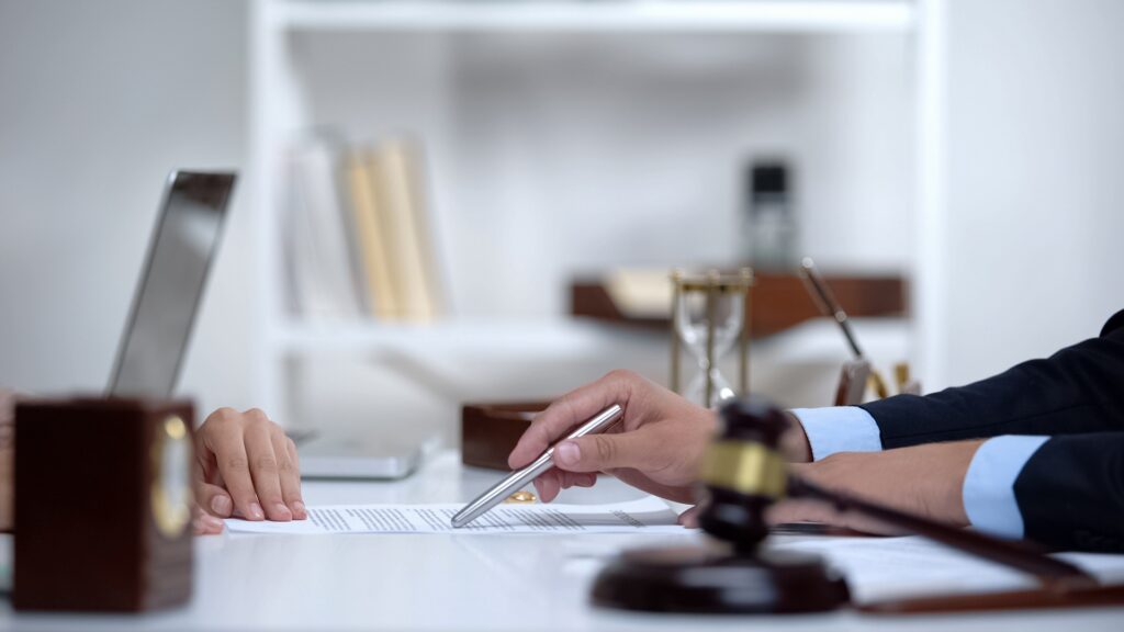An attorney points at a sheet of paper with a silver pen while sitting across from a client.