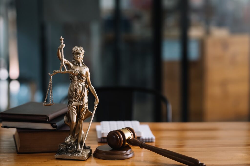 A gavel rests on its side on a wooden desk next to a small statue of lady justice.