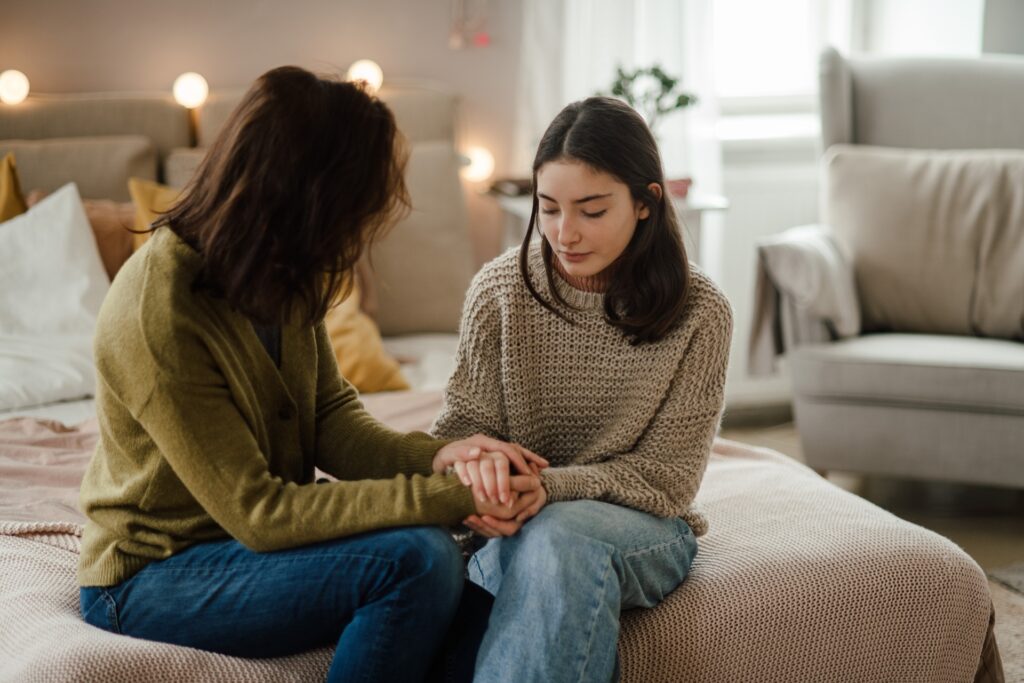 A mother sits with her daughter on a couch with a concerned look on her face.