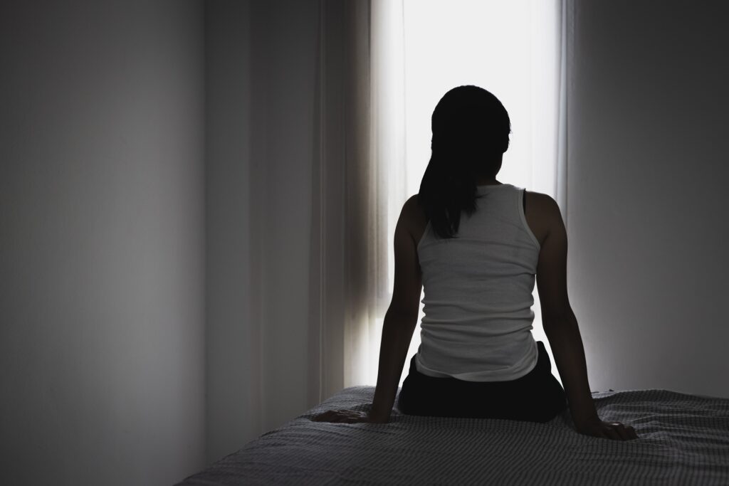 A woman sits on the ground of a darkened hallway.
