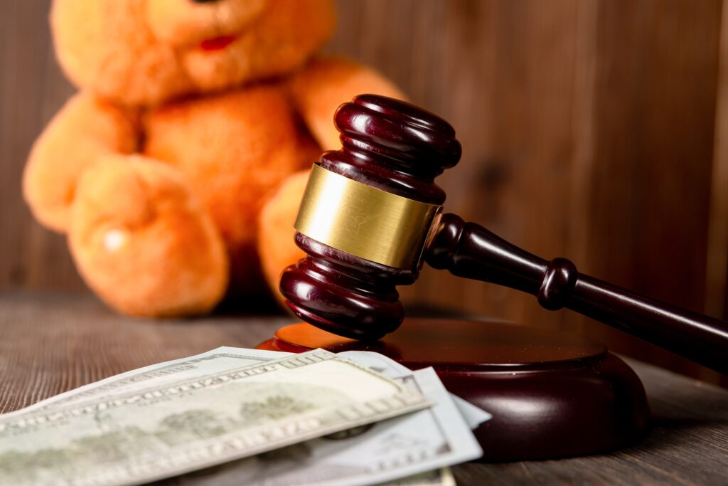 A gavel rests on its stand next to a pile of US currency and a stuffed teddy bear.