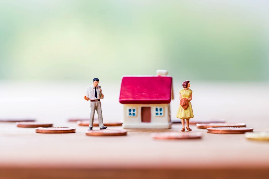 Small figurines of a man and woman standing on coins sit next to a small model house.