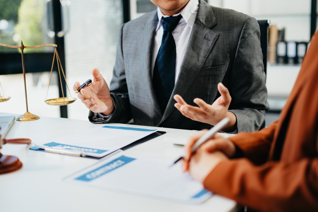 A man in a business suit talks expressively with his hands to a person sitting next to him.