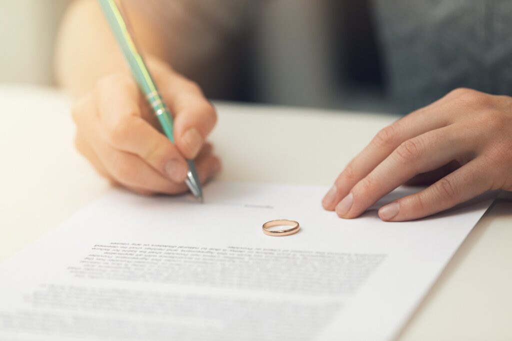 A person signing a document with a pen with a gold ring sitting on the paper.