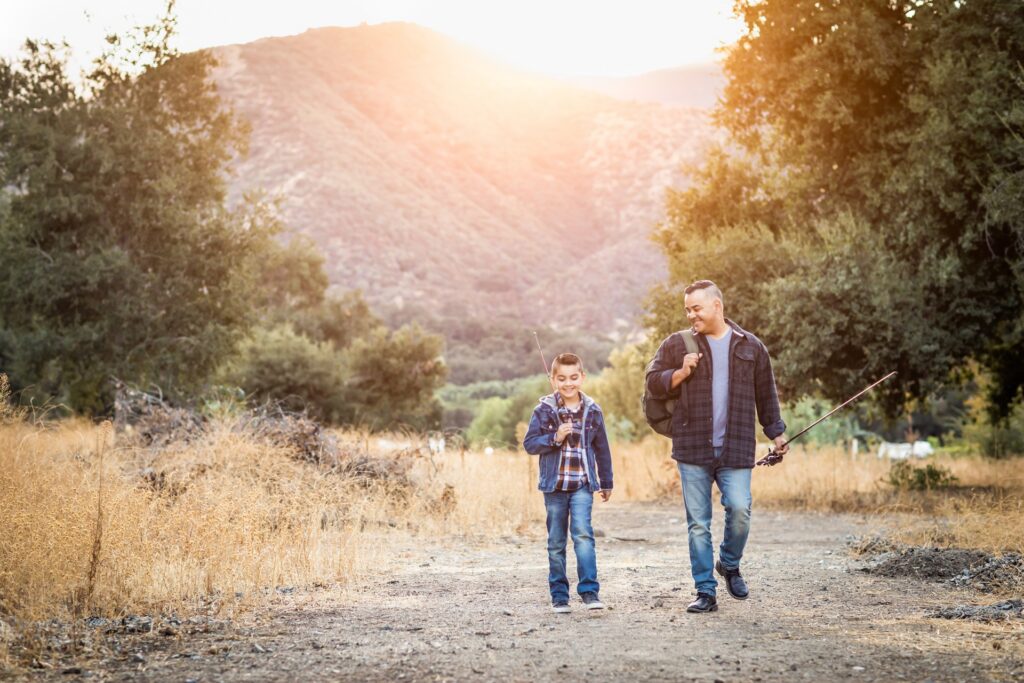 A man walks with his son down a path near trees and a hill.