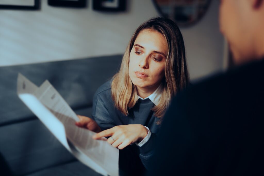 A woman sitting on a couch pointing at a piece of paper.