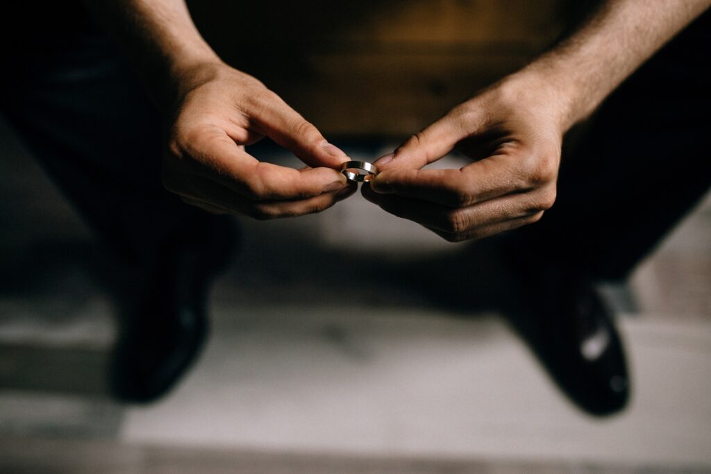 A person holds a wedding ring with both hands while sitting in a darkened room.