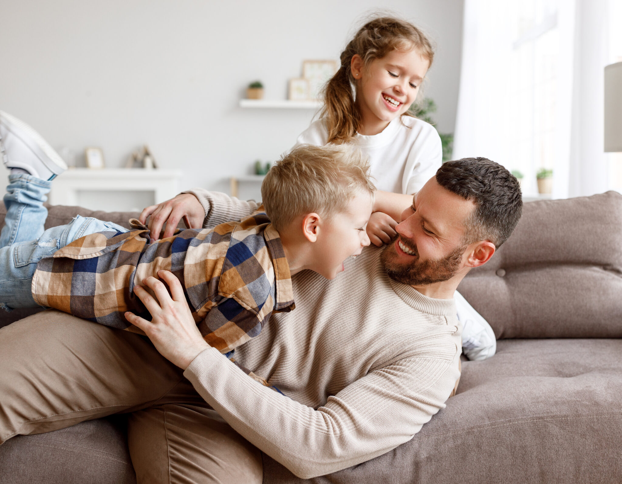 Father laughing and playing with his two children on a sofa | Hemmat Law Group