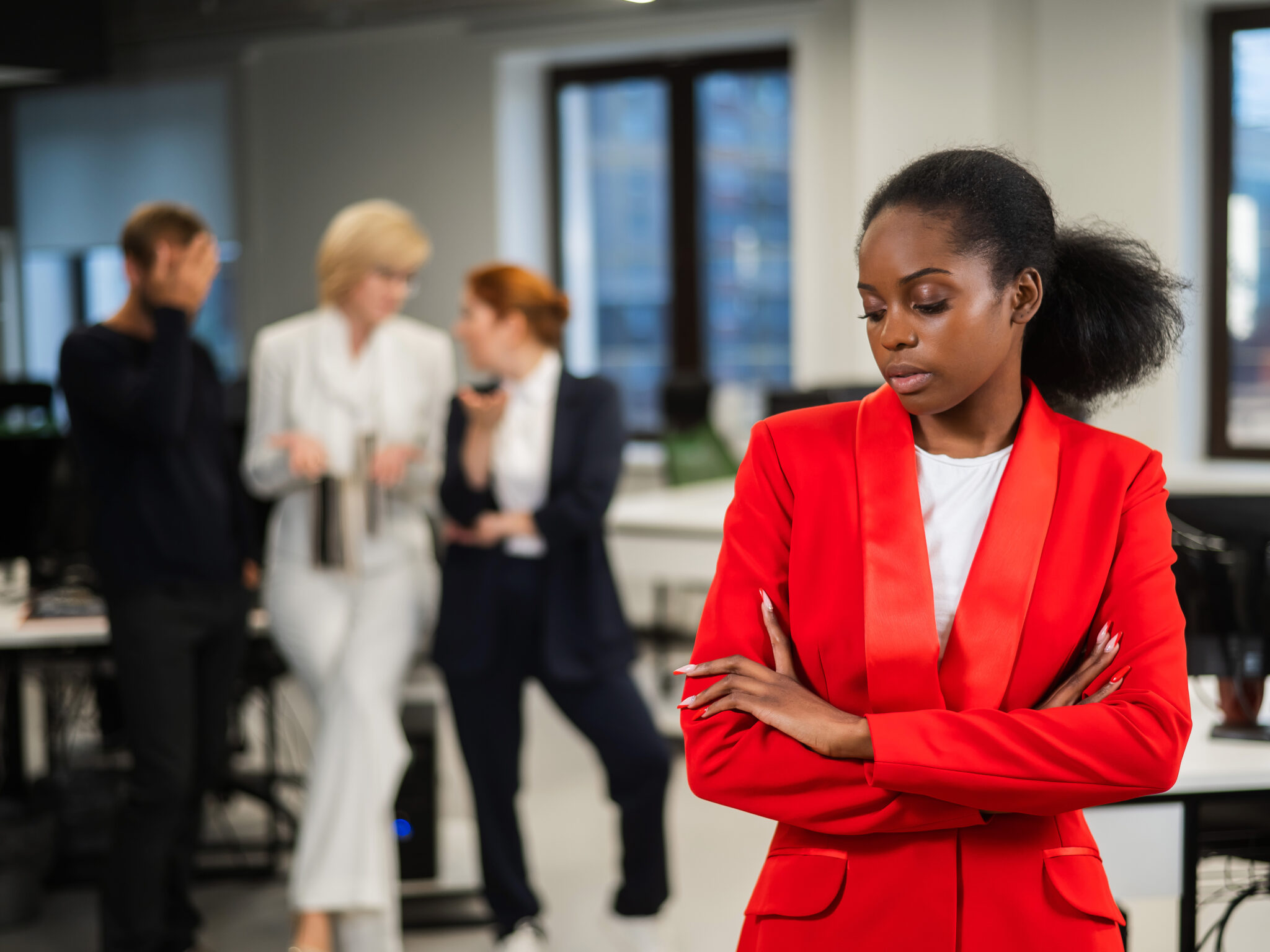 Concerned woman standing apart from coworkers in an office | Hemmat Law Group