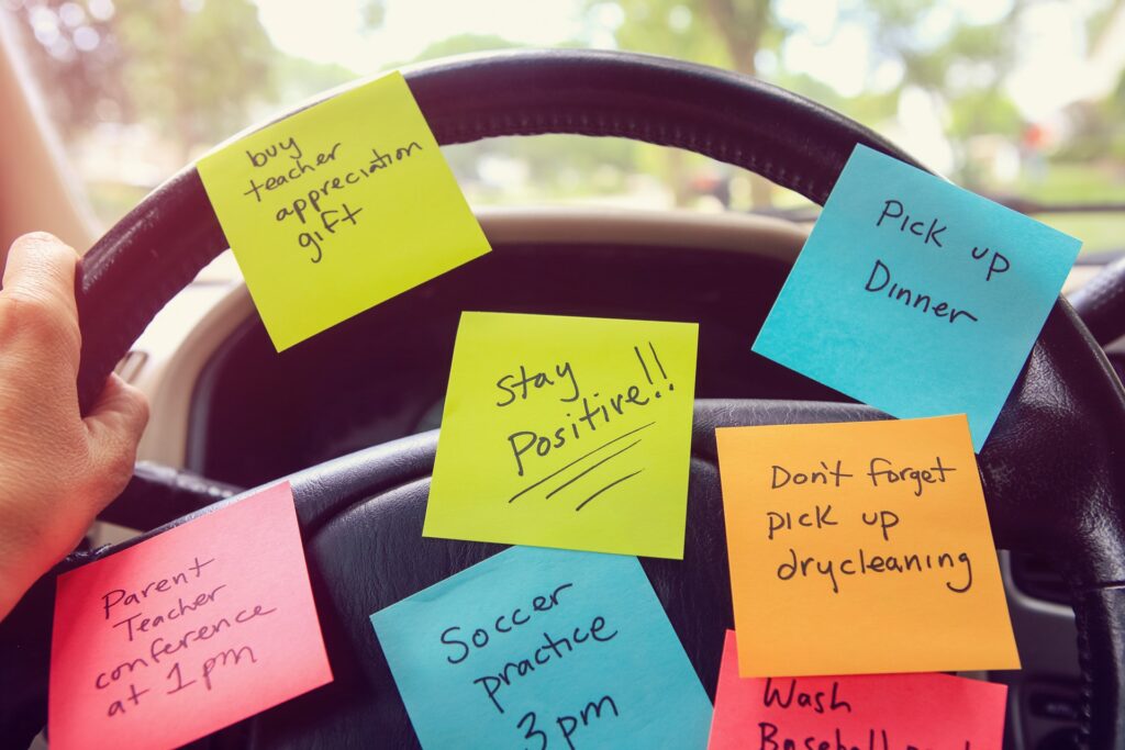 Several colorful post it note reminders on a steering wheel in a car.