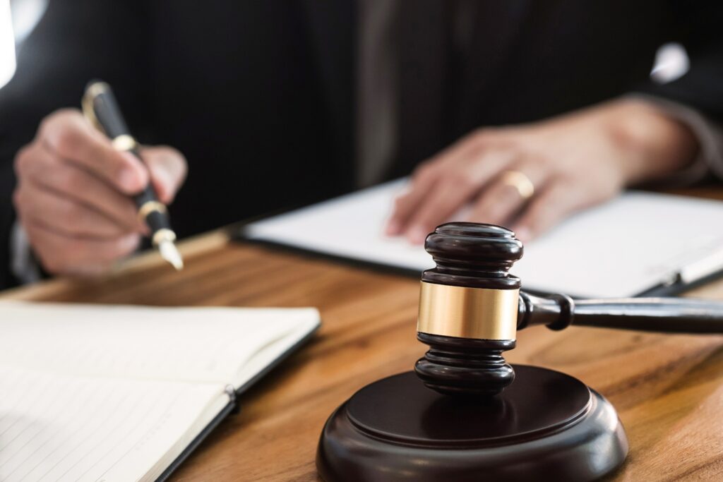 A judge writes on paper with a fountain pen sitting at a wooden desk in front of a gavel resting on its stand.