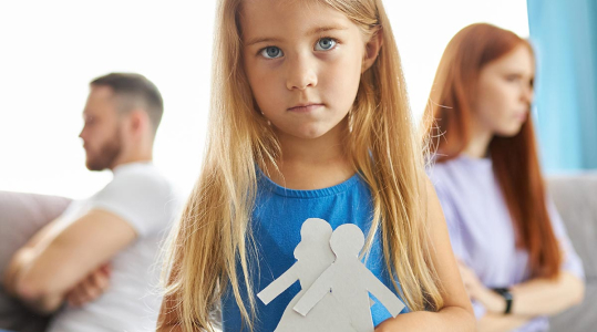 Young girl standing between separated parents at home | Hemmat Law Group