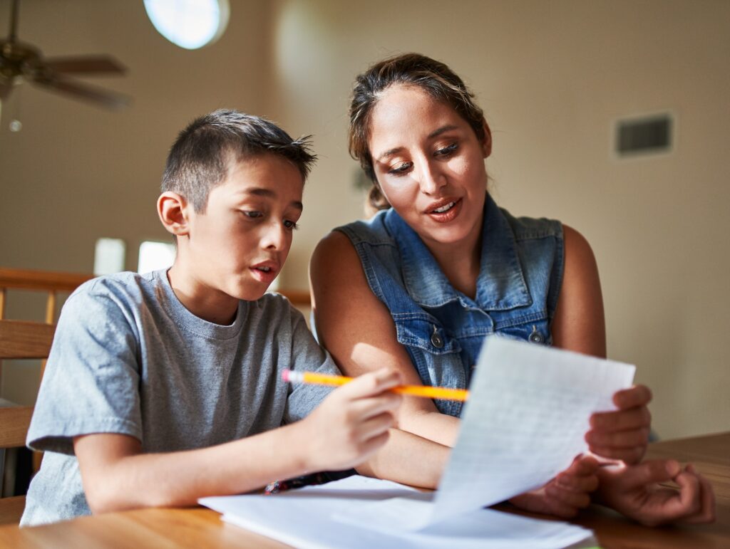 A mother looks at homework with her son at a table.