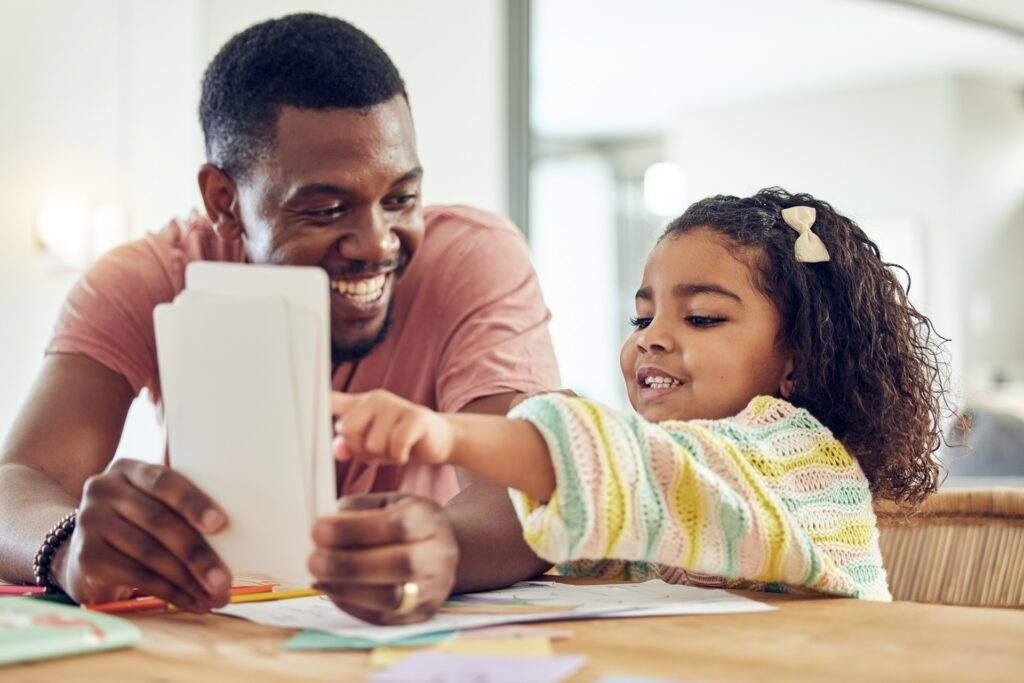 A father smiles at his daughter while holding a piece of paper.