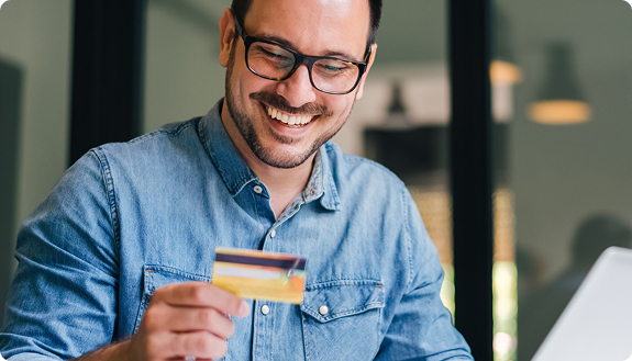 Smiling man holding a payment card beside his laptop | Hemmat Law Group