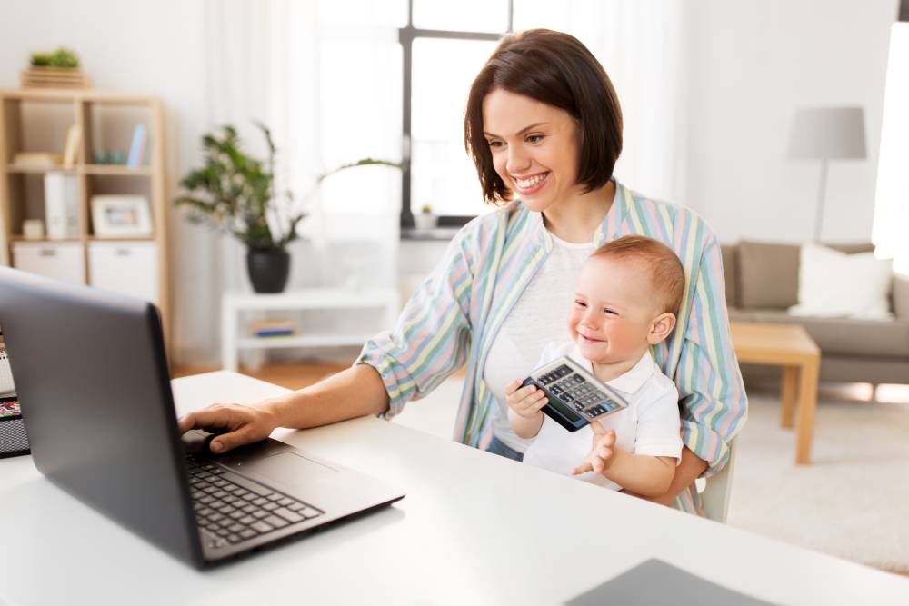 Mother working on laptop while holding her baby | Hemmat Law Group