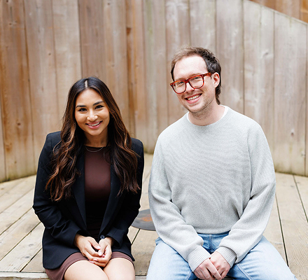 Two smiling professionals seated together against wood wall | Hemmat Law Group