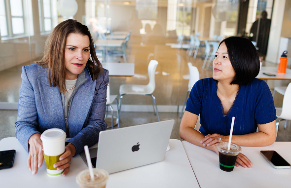 Two women discussing work over coffee and a laptop | Hemmat Law Group
