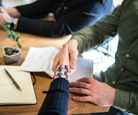 Two people shaking hands across an office meeting table | Hemmat Law Group