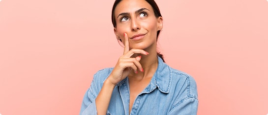 Thoughtful woman in denim shirt against a pink background | Hemmat Law Group