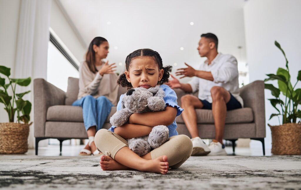 Distressed child holding toy as parents argue behind her | Hemmat Law Group