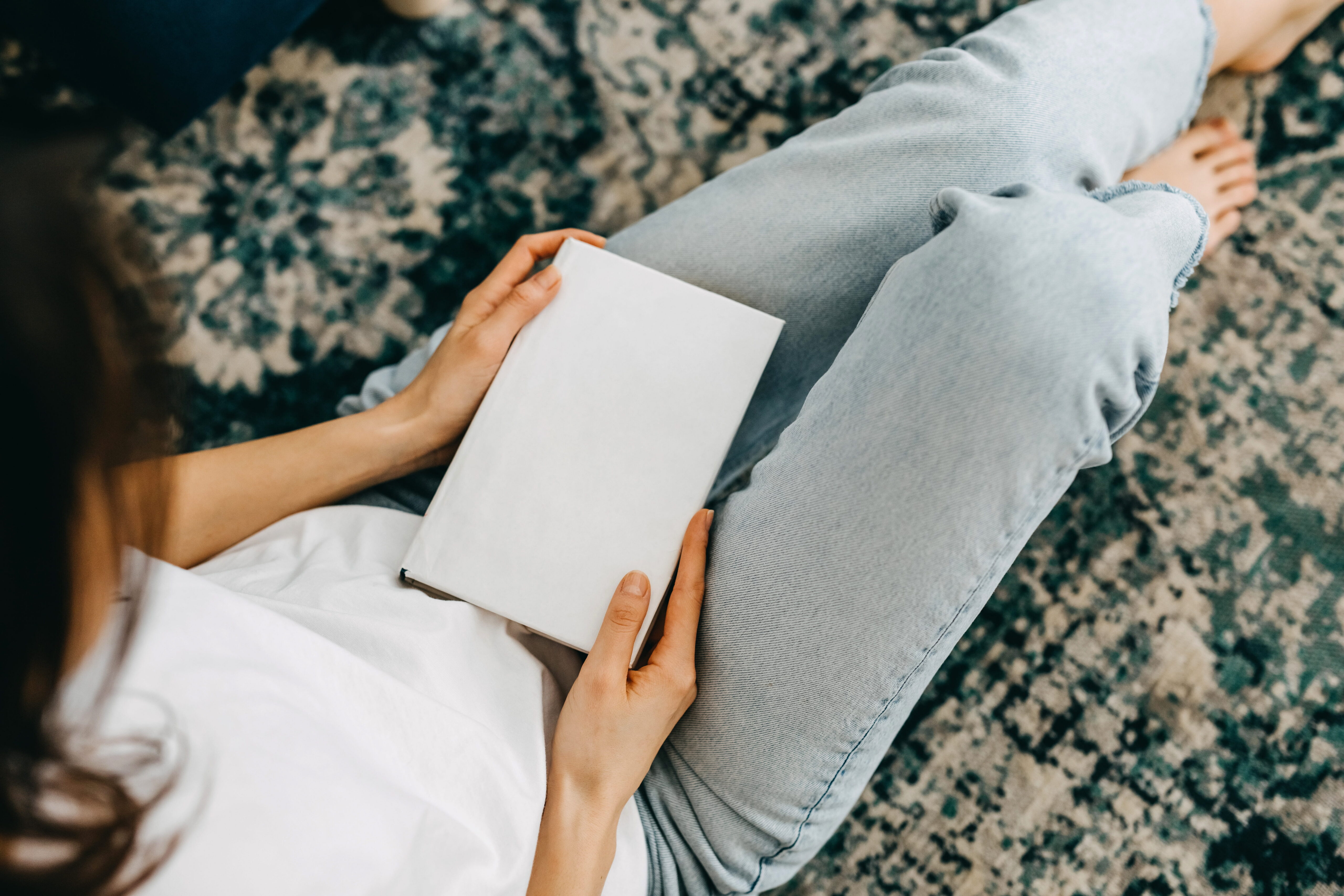 Woman sitting on floor while reading a book at home | Hemmat Law Group