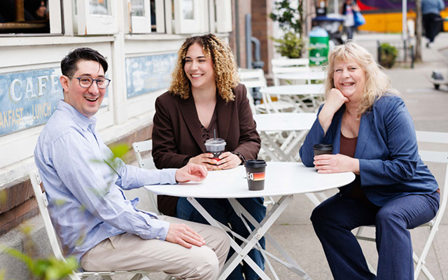 Three people smiling together at an outdoor café table | Hemmat Law Group