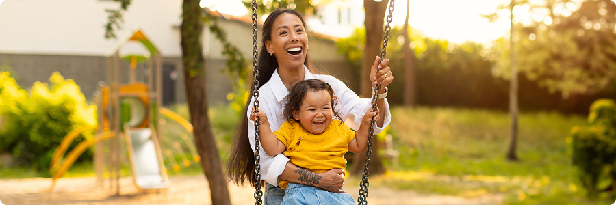 Mother & young child smiling together on a playground swing | Hemmat Law Group