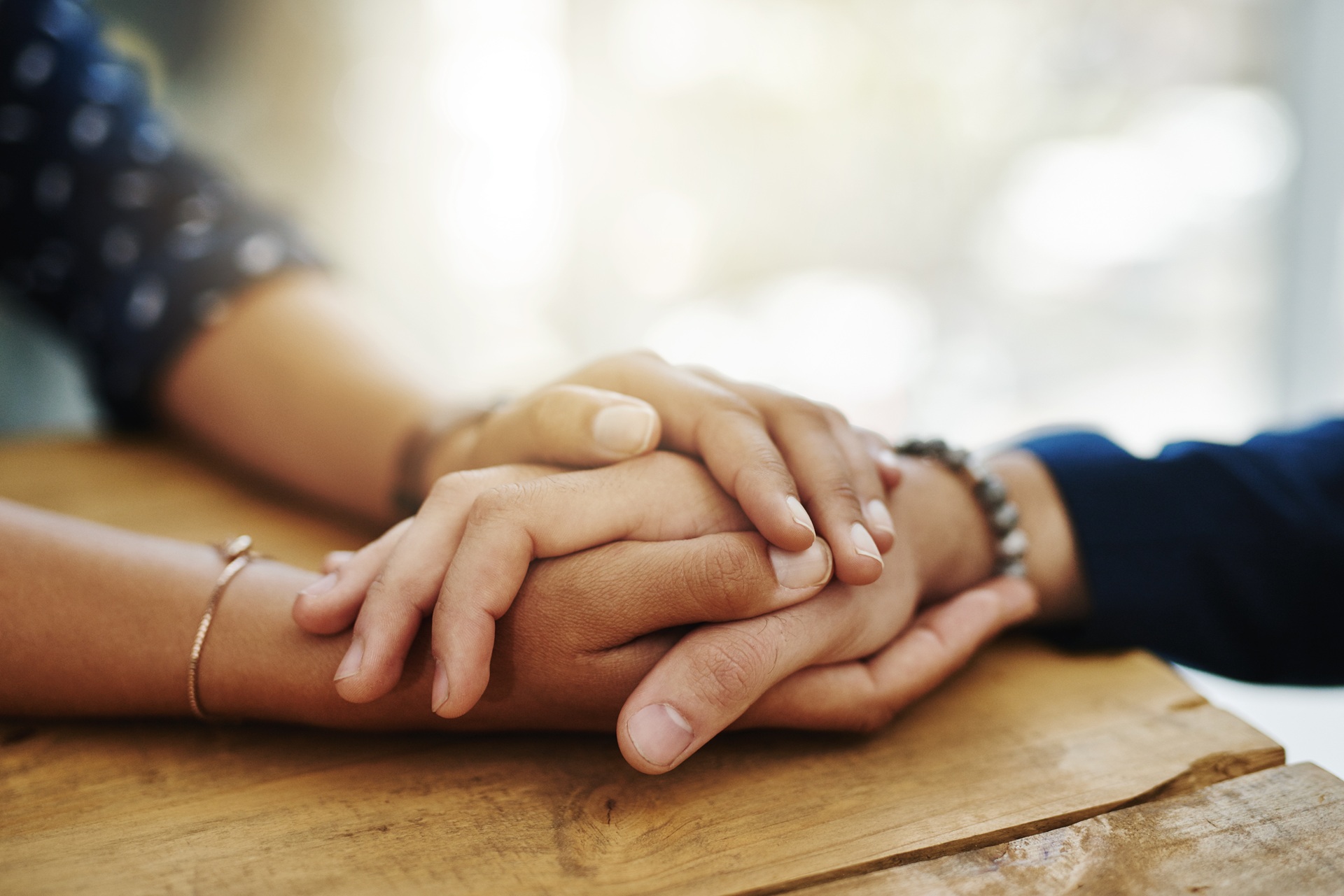 Comforting hands clasped on wood table | Hemmat Law Group